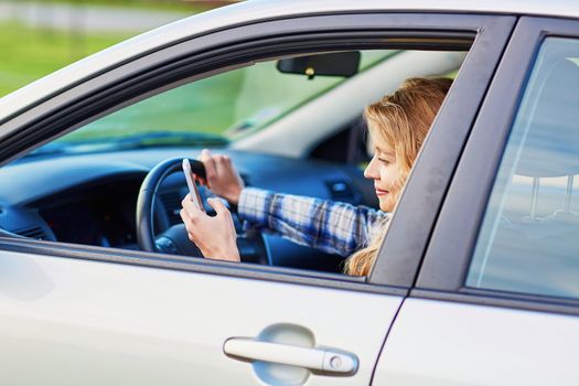 Young woman using her smartphone while driving a car
