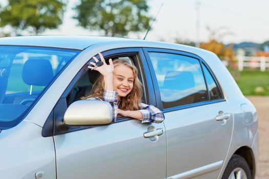 Beautiful young driver looking out of the car window holding a key