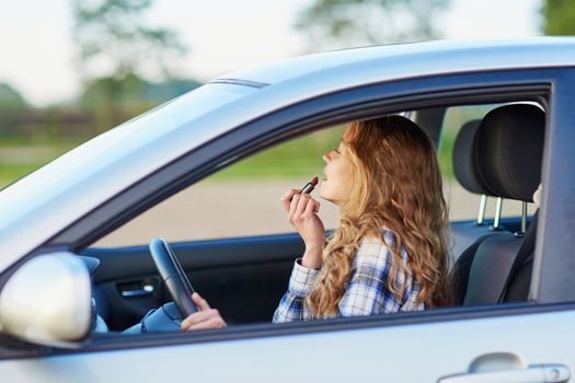 Beautiful blond woman applying lipstick in a car while driving