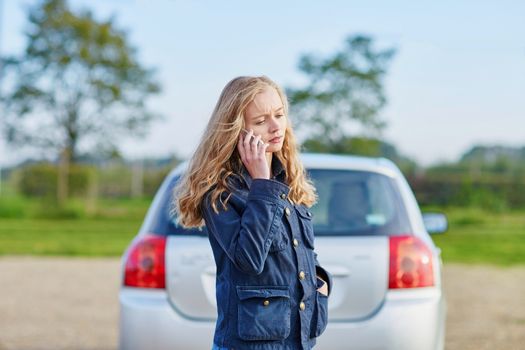 Young woman on the road near a broken car calling for help