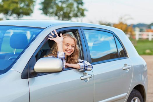 Beautiful young driver looking out of the car window holding a key