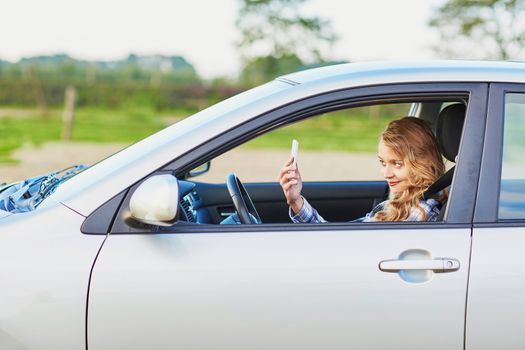 Young woman using her smartphone and making selfie while driving a car