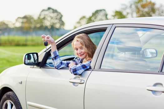 Beautiful young driver looking out of the car window holding a key