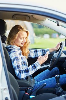 Young woman using her smartphone while driving a car