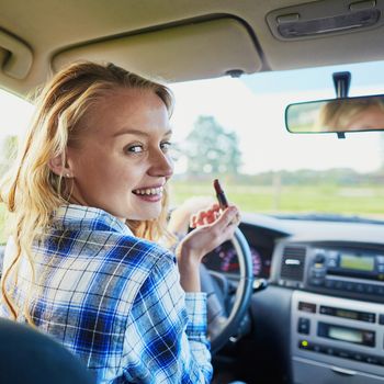 Beautiful blond woman applying lipstick in a car while driving