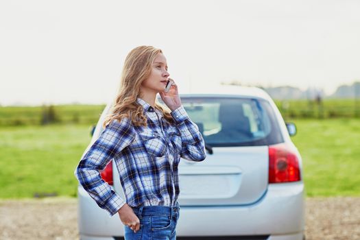 Young woman on the road near a broken car calling for help