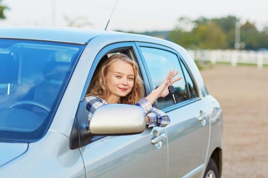 Beautiful young driver looking out of the car window holding a key