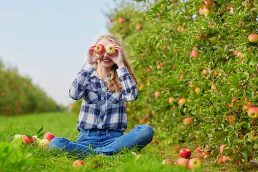 Beautiful young woman having fun with red ripe apples in orchard or on farm on a fall day
