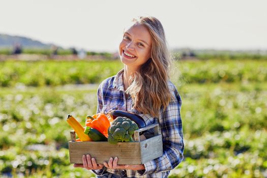 Happy young woman holding wooden crate with fresh organic vegetables from farm