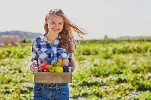 Happy young woman holding wooden crate with fresh organic vegetables from farm