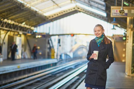 Beautiful young woman waiting for a train while drinking coffee on the platform of Parisian underground