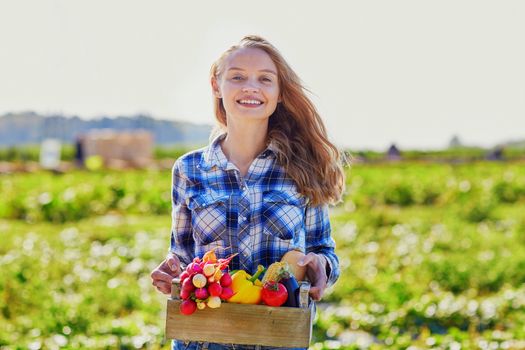 Woman holding wooden crate with fresh organic vegetables from farm