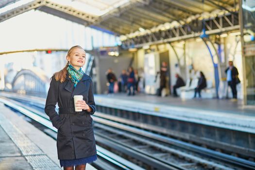 Beautiful young woman waiting for a train while drinking coffee on the platform of Parisian underground