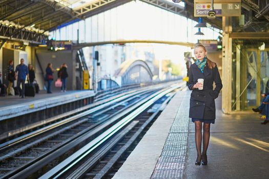 Beautiful young woman waiting for a train while drinking coffee on the platform of Parisian underground