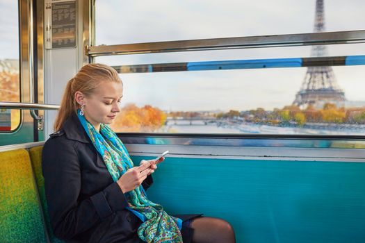 Beautiful young woman travelling in a train of Parisian underground and using her mobile phone. Eiffel tower is behind the window
