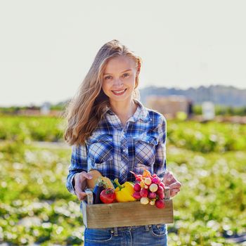 Woman holding wooden crate with fresh organic vegetables from farm