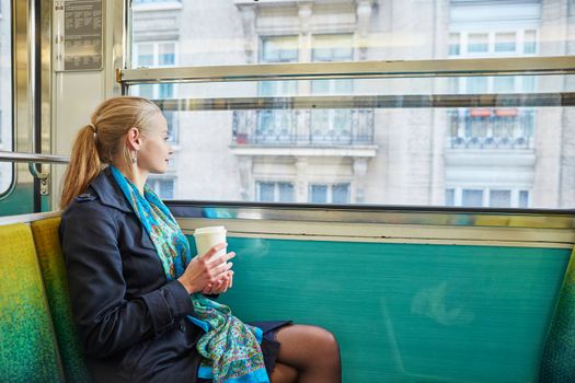 Beautiful young woman travelling in a train of Parisian underground and drinking coffee
