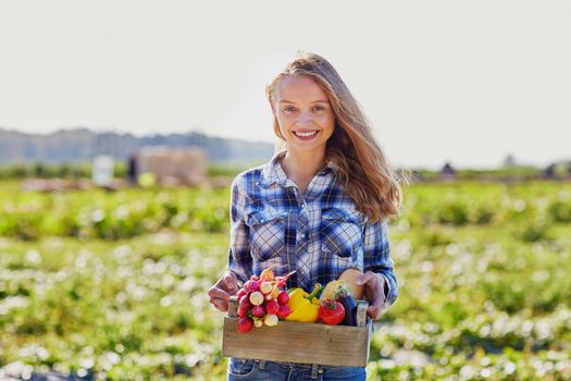 Woman holding wooden crate with fresh organic vegetables from farm