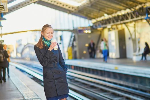 Beautiful young woman waiting for a train while drinking coffee on the platform of Parisian underground