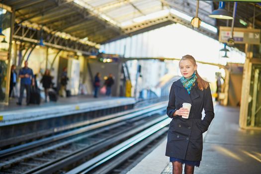 Beautiful young woman waiting for a train while drinking coffee on the platform of Parisian underground