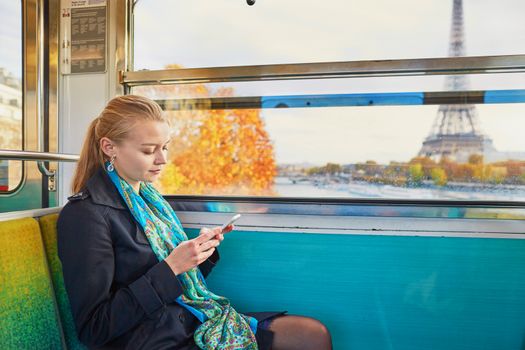 Beautiful young woman travelling in a train of Parisian underground and using her mobile phone. Eiffel tower is behind the window