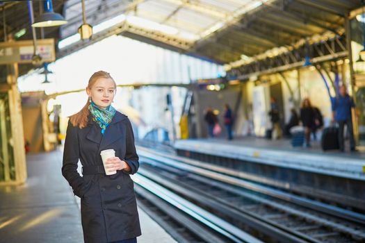 Beautiful young woman waiting for a train while drinking coffee on the platform of Parisian underground