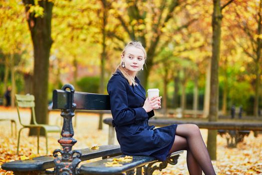 Beautiful young woman in the Luxembourg garden of Paris on a fall day, drinking coffee to go