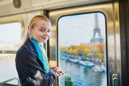Beautiful young woman travelling in a train of Parisian underground and using her mobile phone. Eiffel tower is behind the window