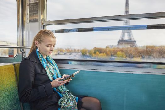 Beautiful young woman travelling in a train of Parisian underground and reading a book. Eiffel tower is behind the window