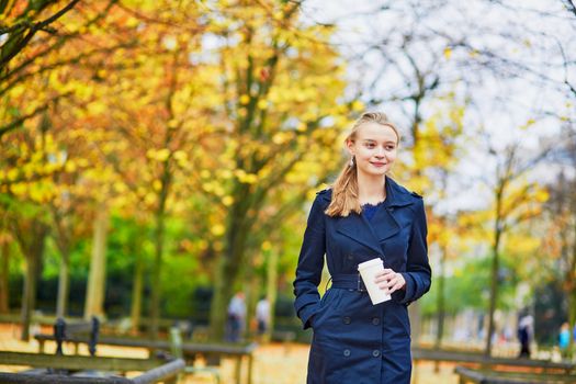 Beautiful young woman in the Luxembourg garden of Paris on a fall day, drinking coffee to go