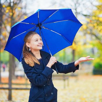 Beautiful young woman with blue umbrella in the Luxembourg garden of Paris on a fall or spring rainy day