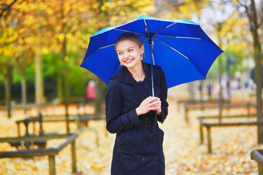Beautiful young woman with blue umbrella in the Luxembourg garden of Paris on a fall or spring rainy day