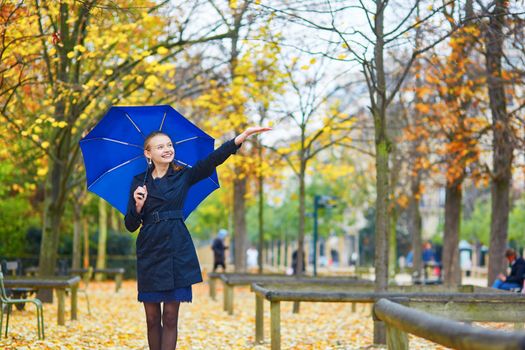 Beautiful young woman with blue umbrella in the Luxembourg garden of Paris on a fall or spring rainy day