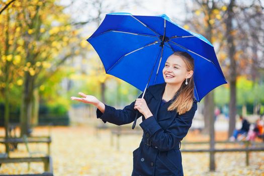 Beautiful young woman with blue umbrella in the Luxembourg garden of Paris on a fall or spring rainy day