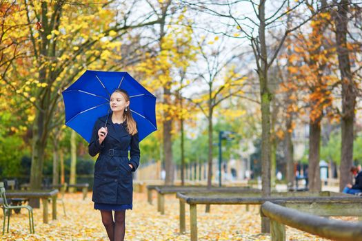 Beautiful young woman with blue umbrella in the Luxembourg garden of Paris on a fall or spring rainy day