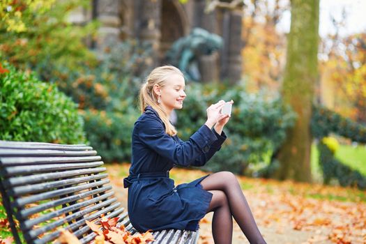 Beautiful young woman on a street of Paris on a sunny fall or spring day taking selfie with her mobile phone