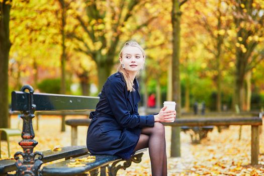 Beautiful young woman in the Luxembourg garden of Paris on a fall day, drinking coffee to go