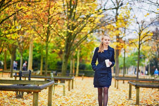 Beautiful young woman in the Luxembourg garden of Paris on a fall day, drinking coffee to go