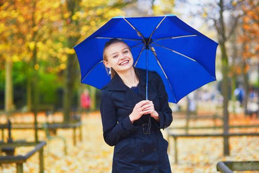 Beautiful young woman with blue umbrella in the Luxembourg garden of Paris on a fall or spring rainy day
