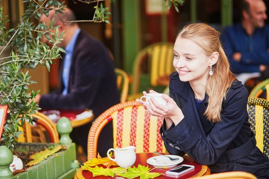 Beautiful young woman drinking hot chocolate in Parisian outdoor cafe on a nice fall day