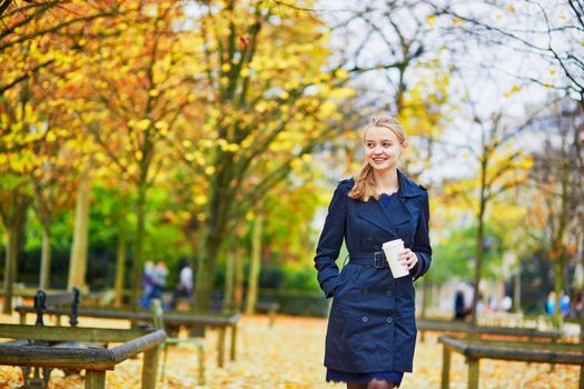 Beautiful young woman in the Luxembourg garden of Paris on a fall day, drinking coffee to go