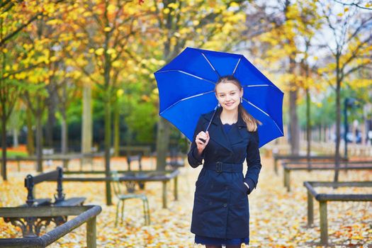Beautiful young woman with blue umbrella in the Luxembourg garden of Paris on a fall or spring rainy day