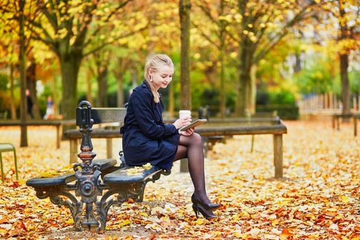 Beautiful young woman in the Luxembourg garden of Paris on a fall day, drinking coffee to go and reading book