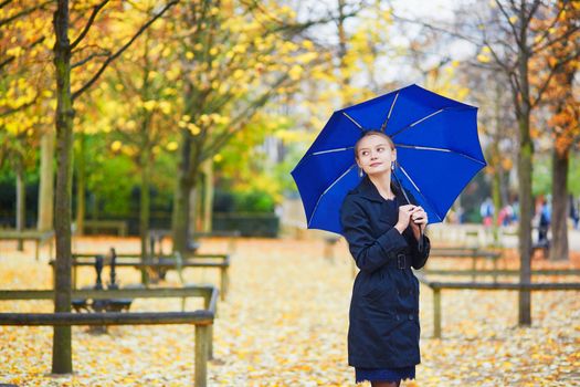 Beautiful young woman with blue umbrella in the Luxembourg garden of Paris on a fall or spring rainy day
