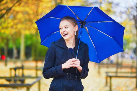 Beautiful young woman with blue umbrella in the Luxembourg garden of Paris on a fall or spring rainy day