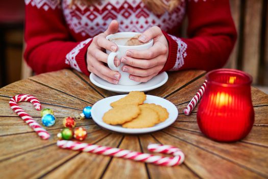 Cheerful young woman drinking hot chocolate in a cozy outdoor Parisian cafe decorated for Christmas