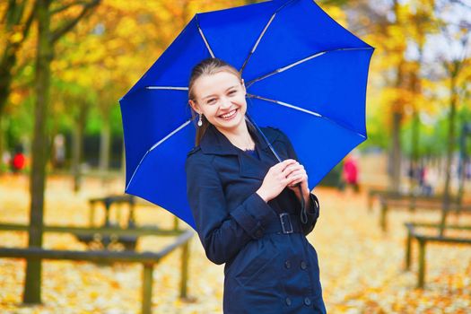 Beautiful young woman with blue umbrella in the Luxembourg garden of Paris on a fall or spring rainy day