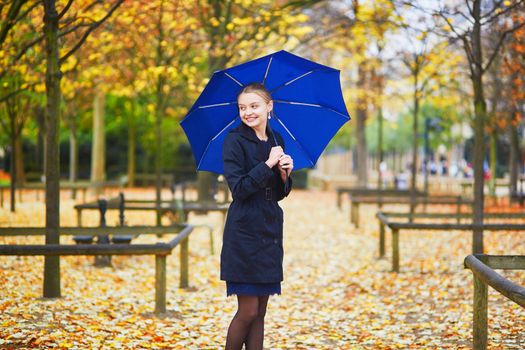 Beautiful young woman with blue umbrella in the Luxembourg garden of Paris on a fall or spring rainy day