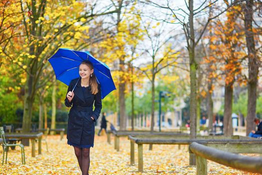 Beautiful young woman with blue umbrella in the Luxembourg garden of Paris on a fall or spring rainy day