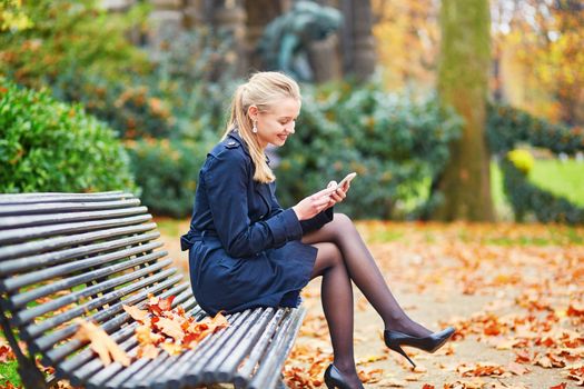 Beautiful young woman on a street of Paris on a sunny fall or spring day taking selfie with her mobile phone